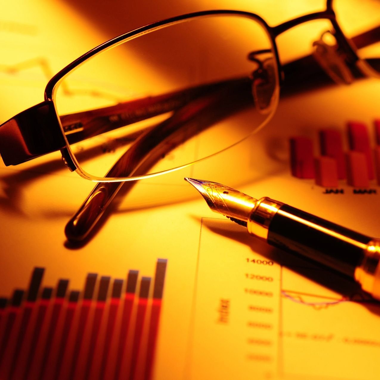 pair of glasses and a pen on a table with business charts